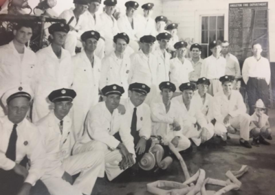 Three rows of firefighters posing with an empty fire hose.