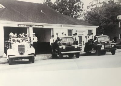 Firefighters posing with three of the department's old firetrucks.
