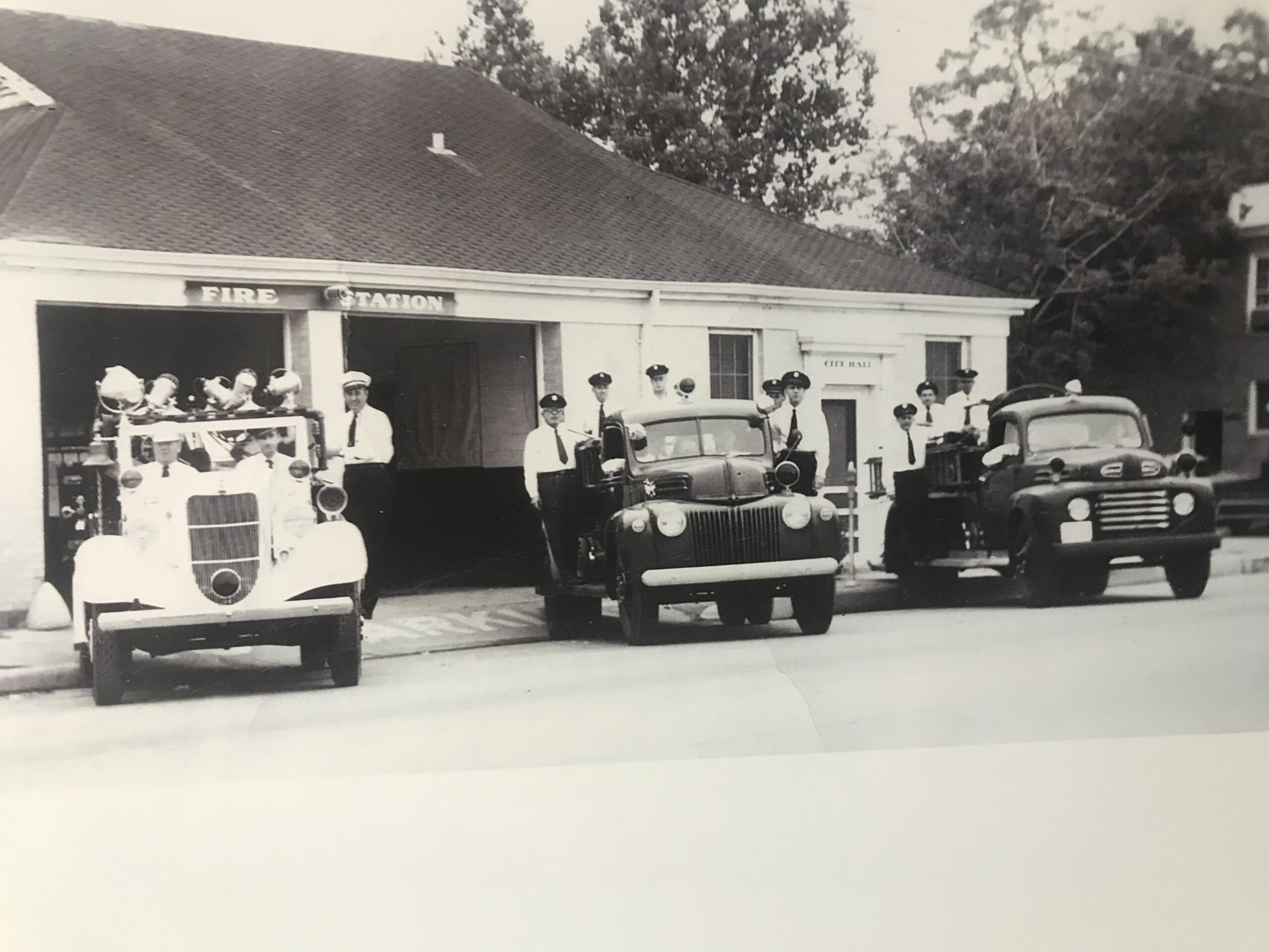 Three Old Firetrucks with Firefighters Firefighters posing with three of the department's old firetrucks.