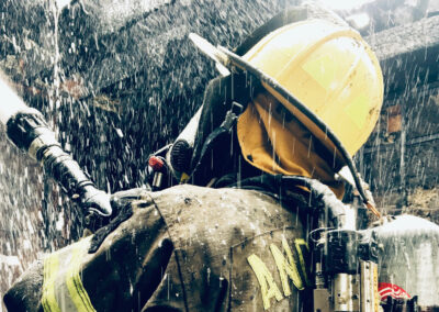 A close up of an Angleton Volunteer Fire Department firefighter spraying water on a burning structure.
